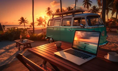 Image of a laptop on a table at the beach at sunset with a VW bus in the background